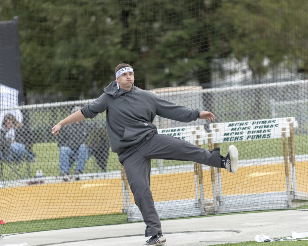 Athlete prepares for pole vault on a track with others watching.