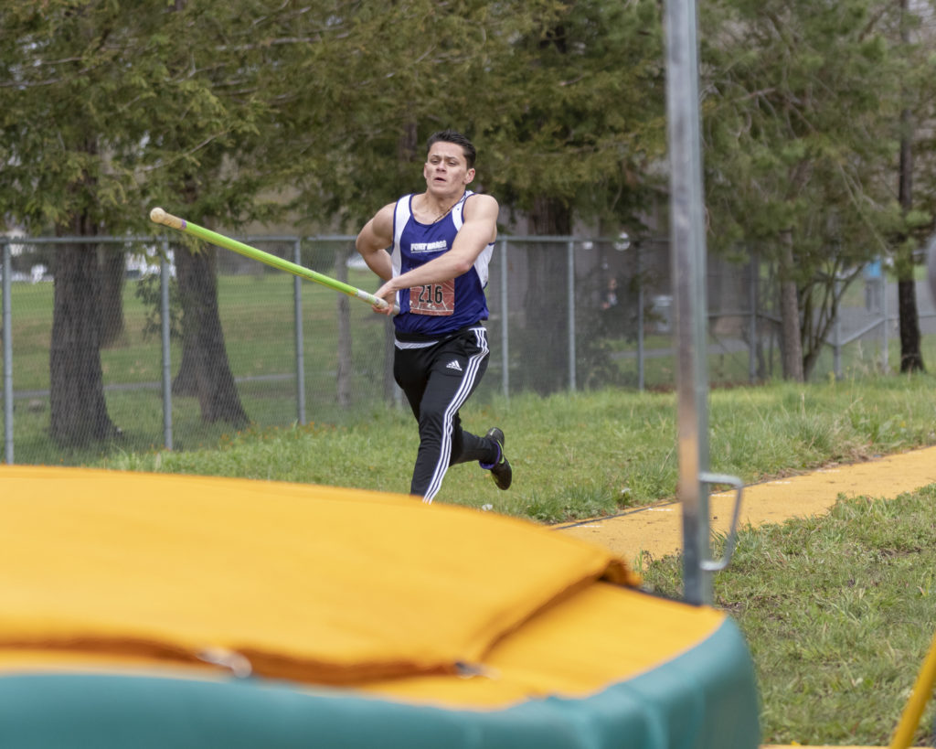 Athlete prepares for pole vault on a track with others watching.