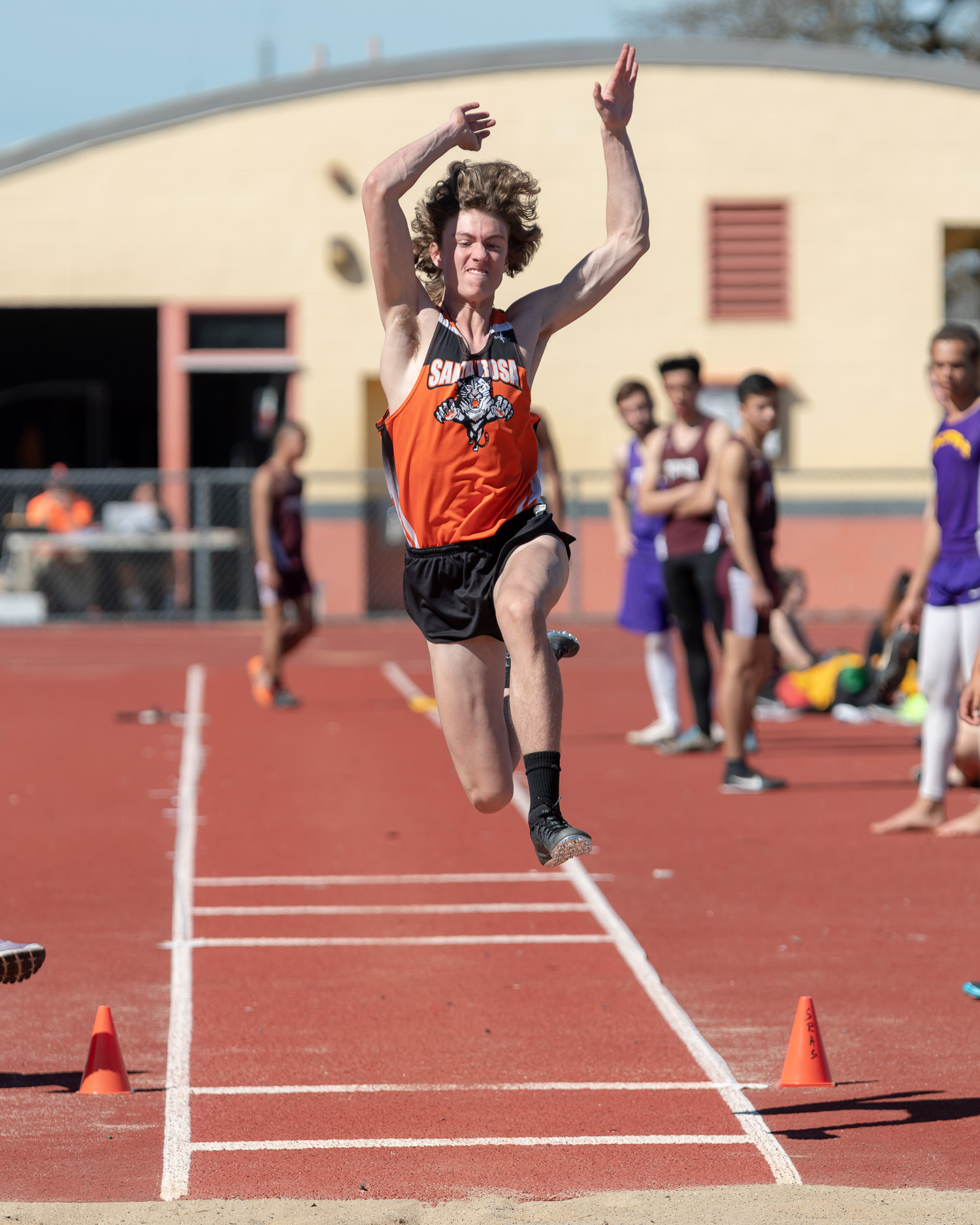Athlete prepares for pole vault on a track with others watching.