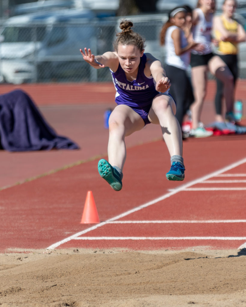 Athlete prepares for pole vault on a track with others watching.