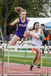 Athlete prepares for pole vault on a track with others watching.