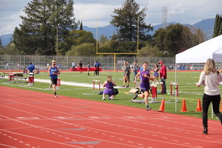 Athlete prepares for pole vault on a track with others watching.