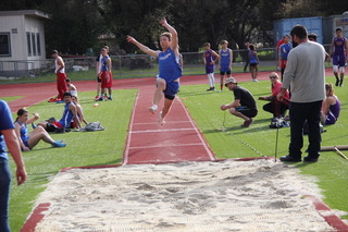 Athlete prepares for pole vault on a track with others watching.
