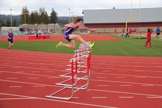 Athlete prepares for pole vault on a track with others watching.