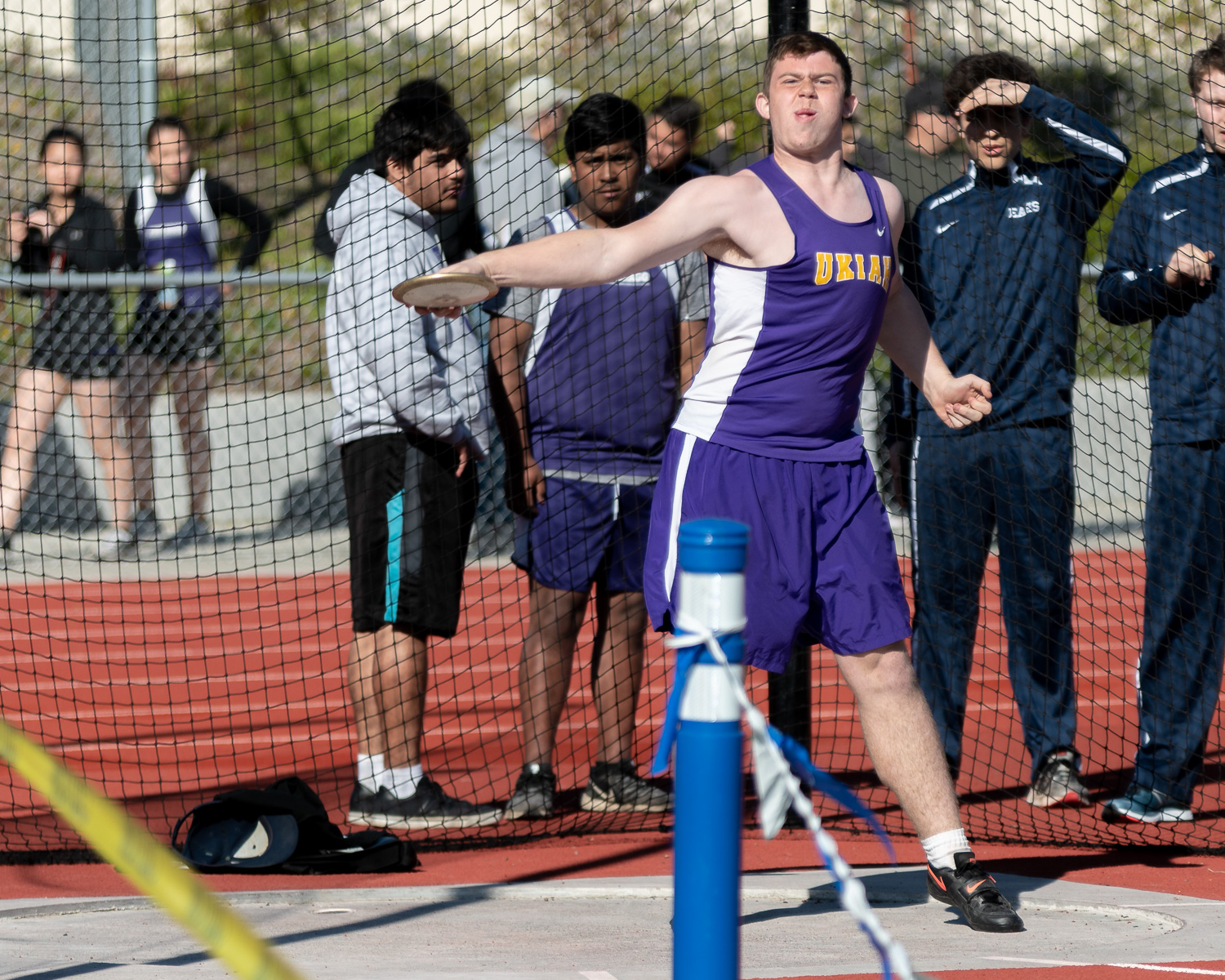 Athlete prepares for pole vault on a track with others watching.