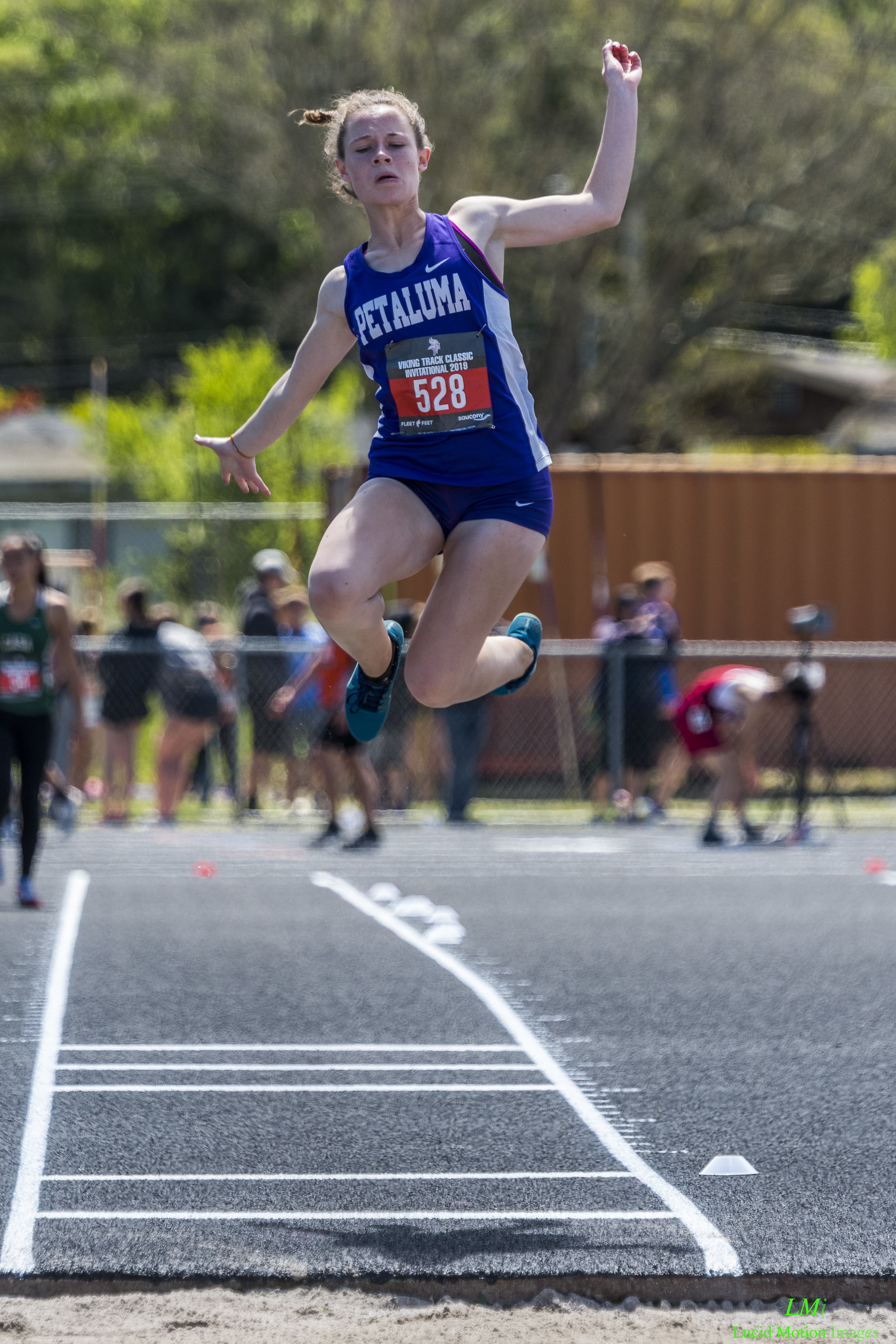 Athlete prepares for pole vault on a track with others watching.