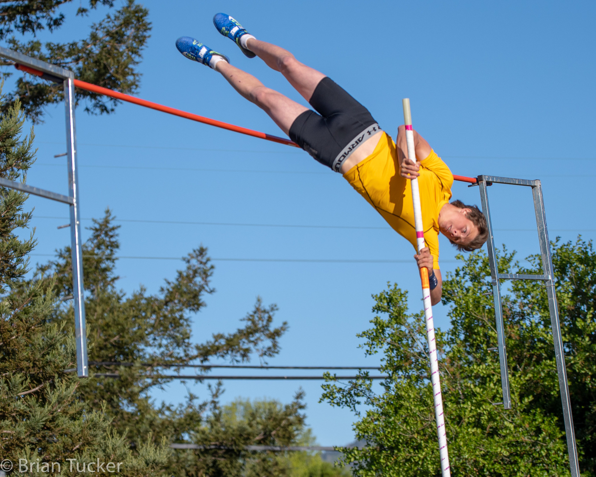 Athlete prepares for pole vault on a track with others watching.