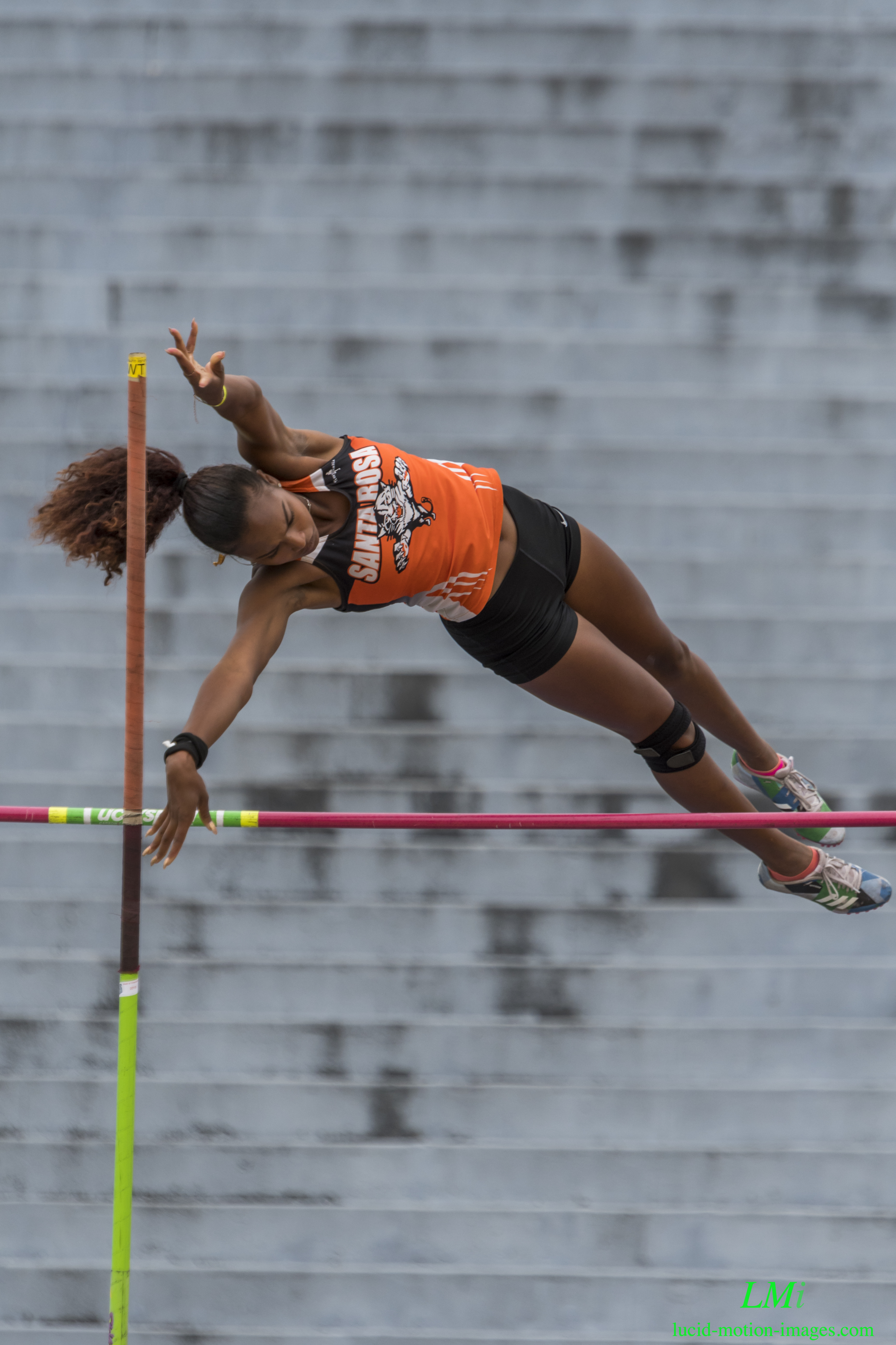 Athlete prepares for pole vault on a track with others watching.