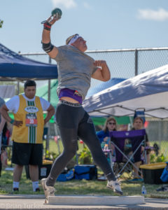 Athlete prepares for pole vault on a track with others watching.