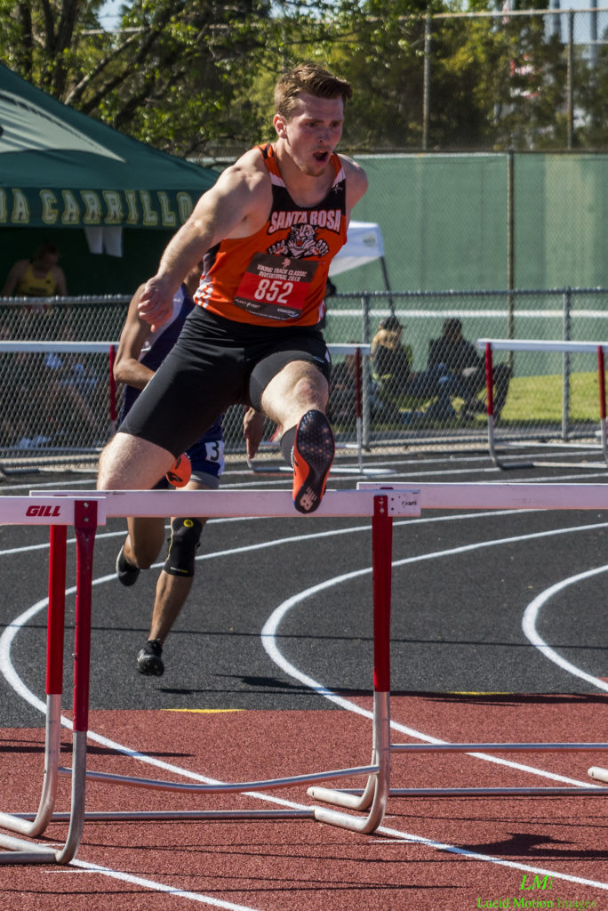 Athlete prepares for pole vault on a track with others watching.