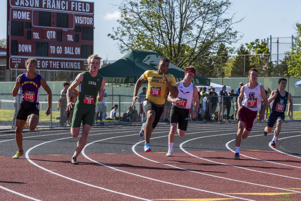 Athlete prepares for pole vault on a track with others watching.