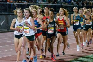 Athlete prepares for pole vault on a track with others watching.
