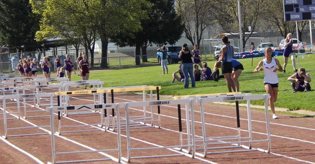 Athlete prepares for pole vault on a track with others watching.