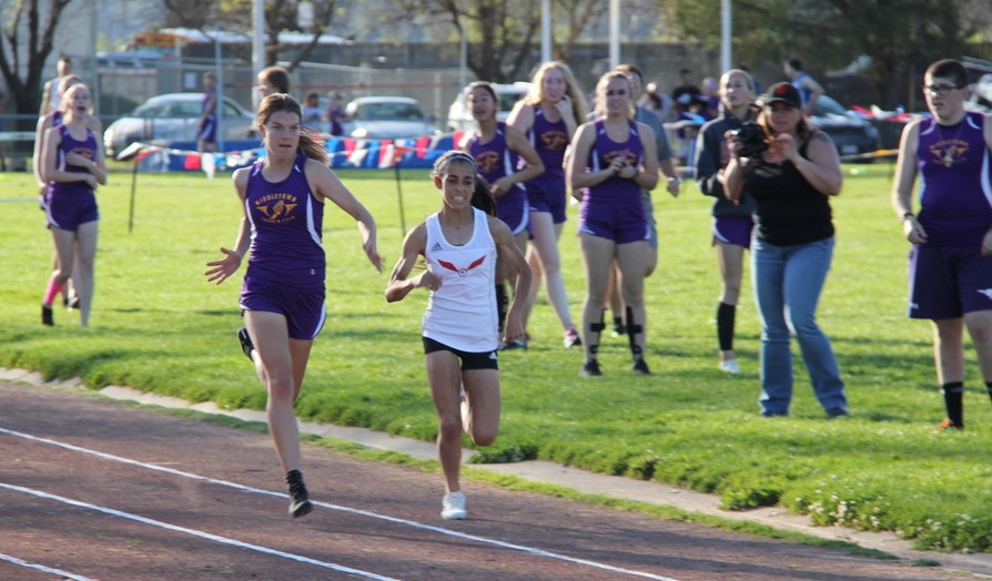 Athlete prepares for pole vault on a track with others watching.