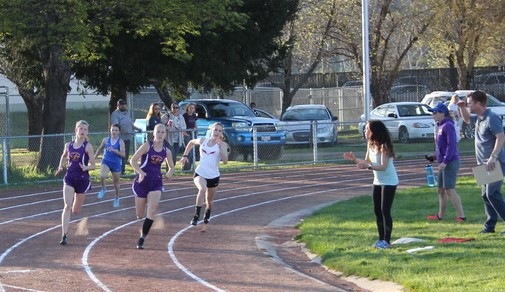 Athlete prepares for pole vault on a track with others watching.