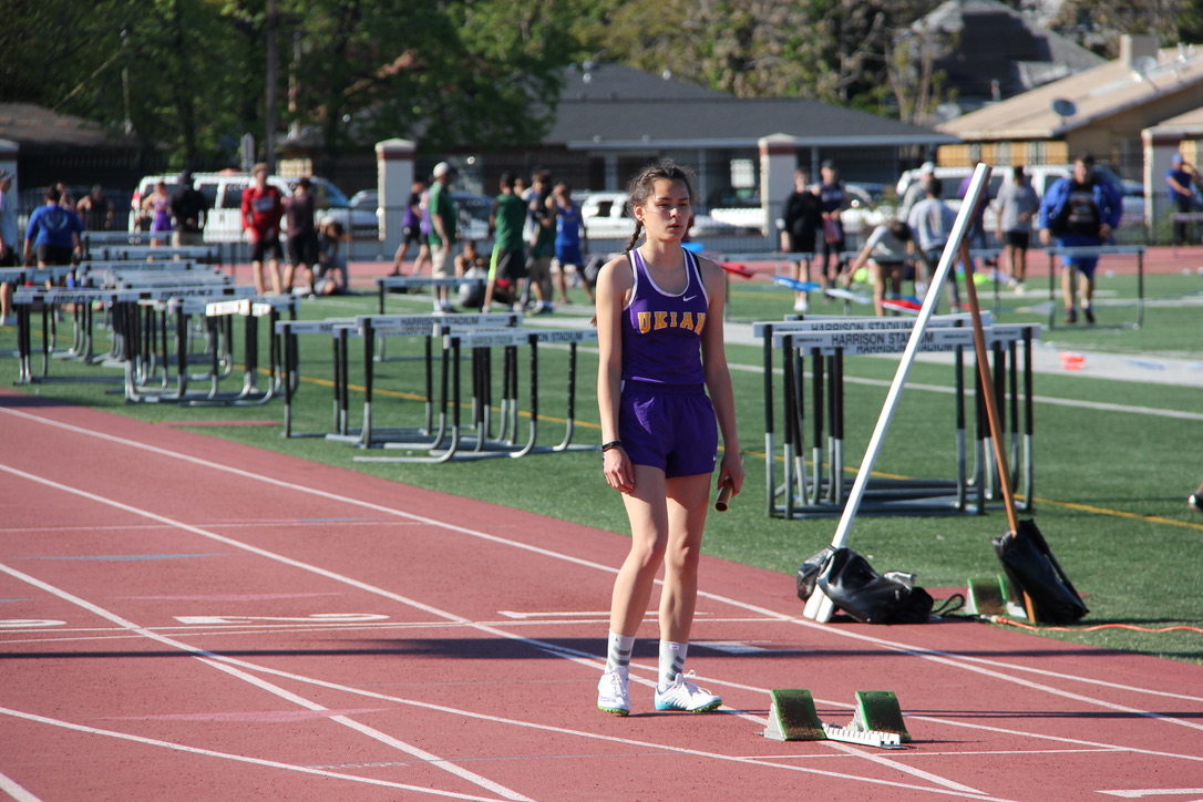 Athlete prepares for pole vault on a track with others watching.