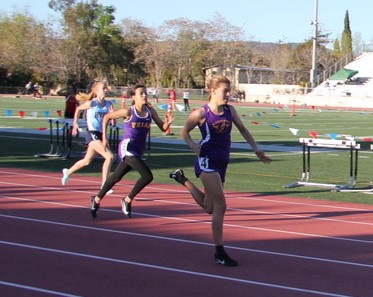 Athlete prepares for pole vault on a track with others watching.