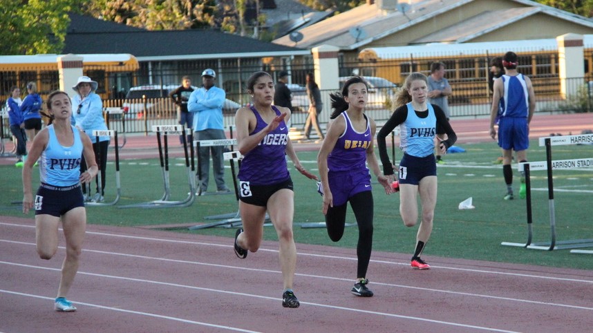 Athlete prepares for pole vault on a track with others watching.