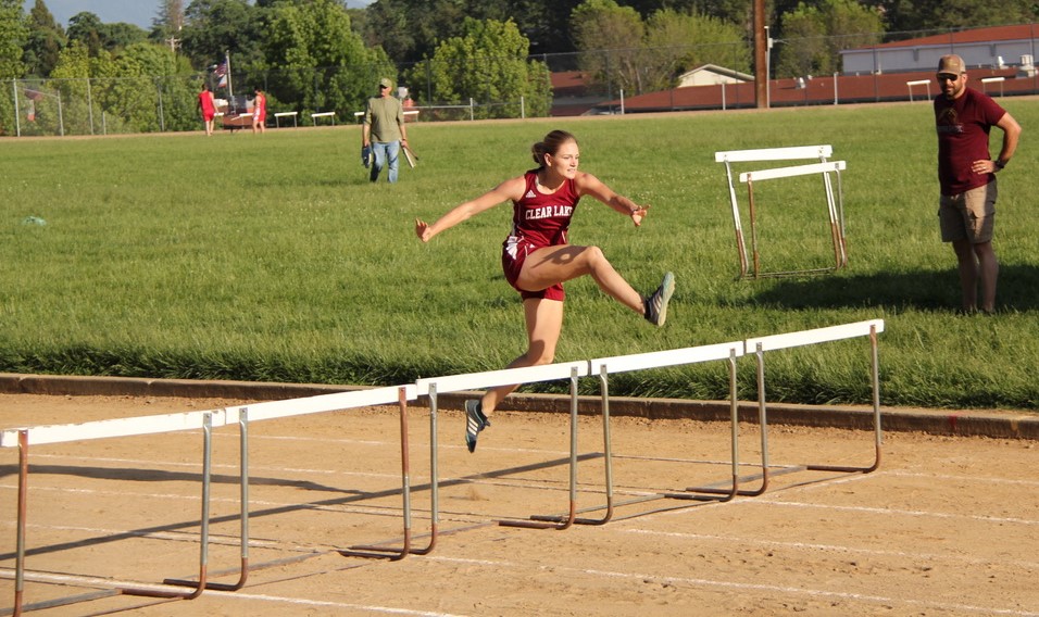 Athlete prepares for pole vault on a track with others watching.