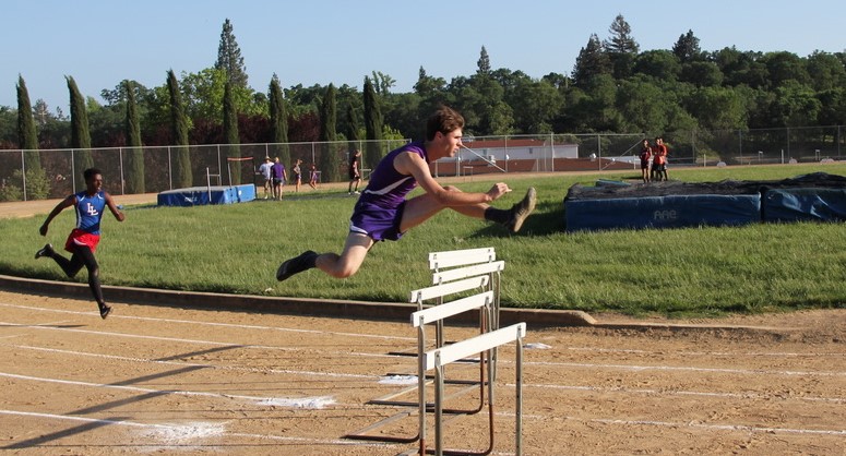 Athlete prepares for pole vault on a track with others watching.
