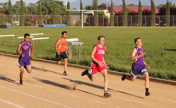Athlete prepares for pole vault on a track with others watching.