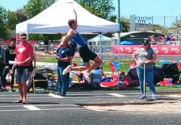 Athlete prepares for pole vault on a track with others watching.
