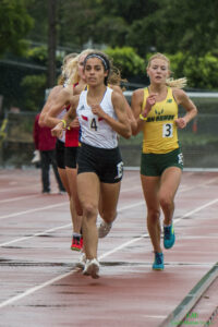 Athlete prepares for pole vault on a track with others watching.