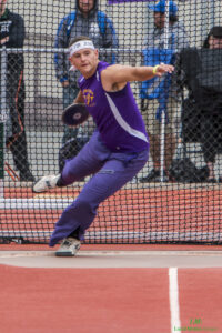 Athlete prepares for pole vault on a track with others watching.