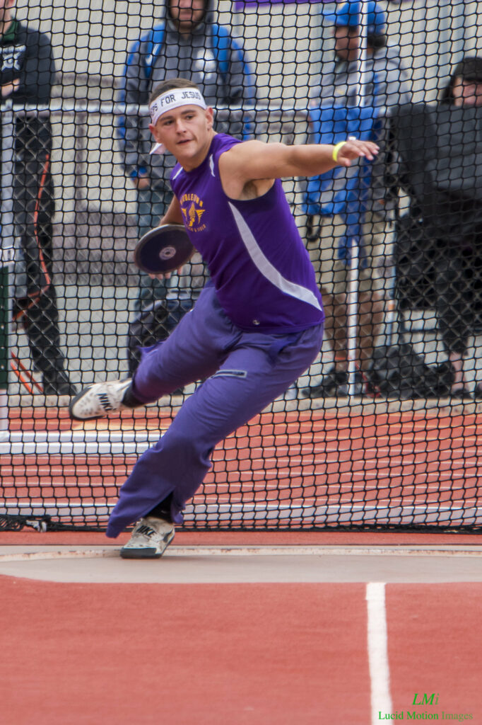 Athlete prepares for pole vault on a track with others watching.