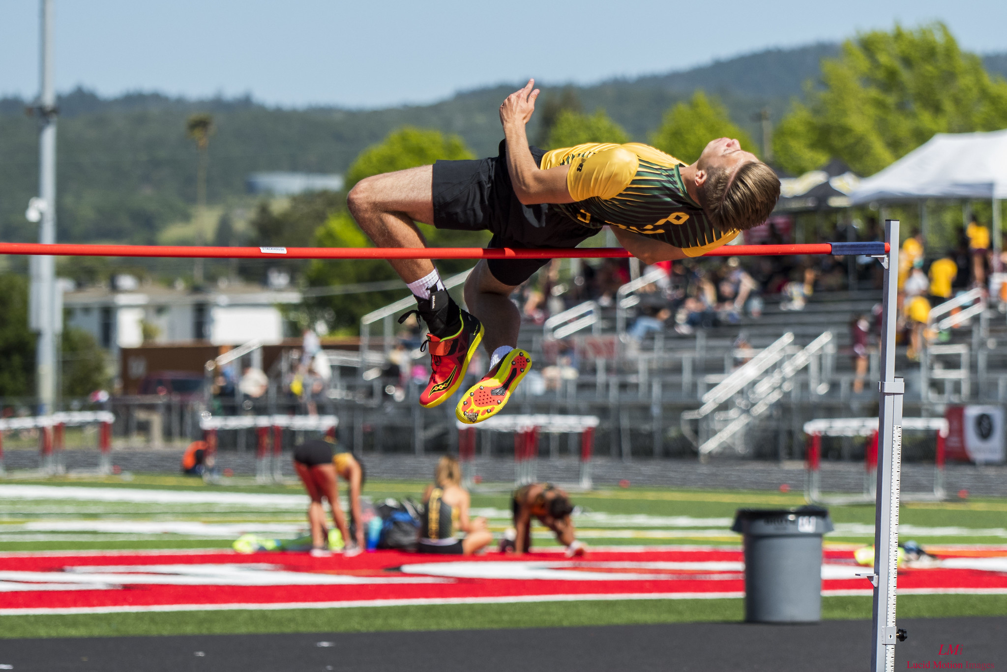 Athlete prepares for pole vault on a track with others watching.