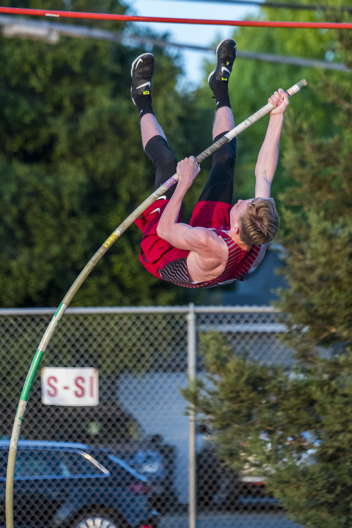 Athlete prepares for pole vault on a track with others watching.