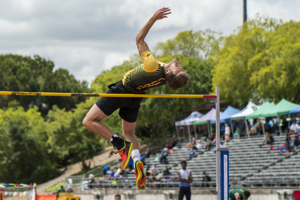 Athlete prepares for pole vault on a track with others watching.