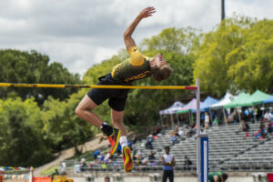 Athlete prepares for pole vault on a track with others watching.