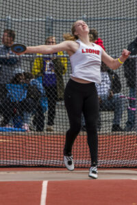 Athlete prepares for pole vault on a track with others watching.