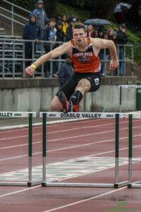 Athlete prepares for pole vault on a track with others watching.