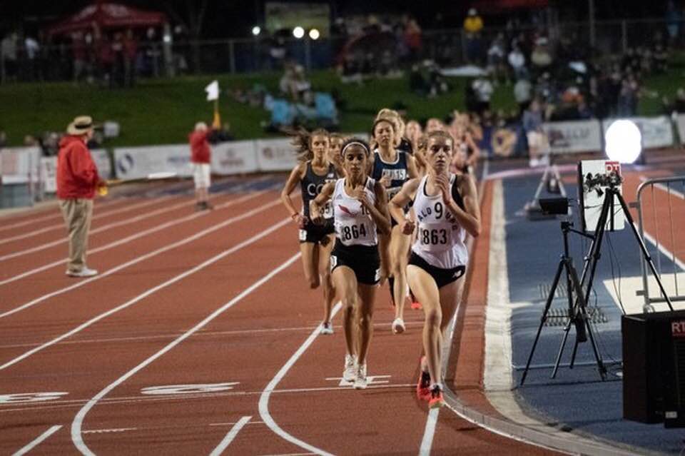 Athlete prepares for pole vault on a track with others watching.