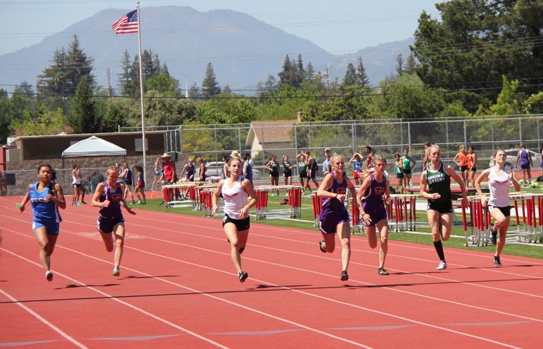 Athlete prepares for pole vault on a track with others watching.