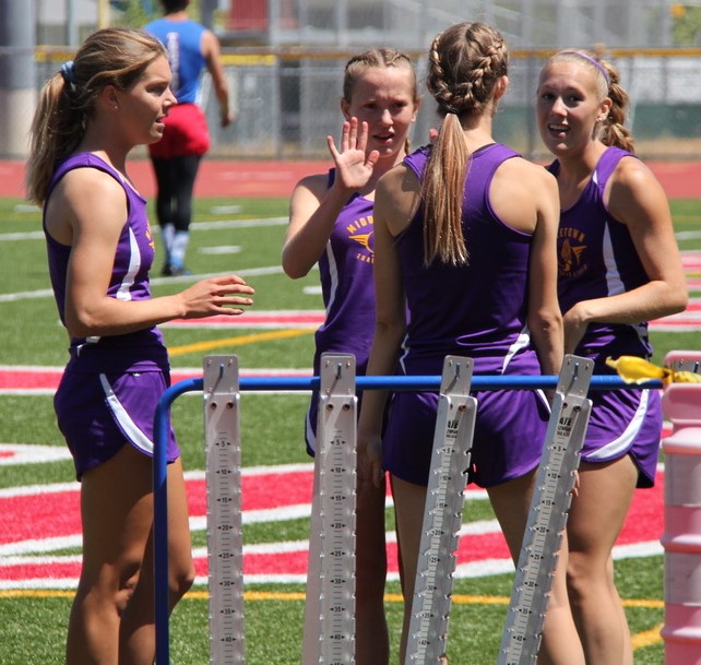 Athlete prepares for pole vault on a track with others watching.