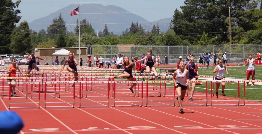 Athlete prepares for pole vault on a track with others watching.