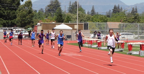 Athlete prepares for pole vault on a track with others watching.