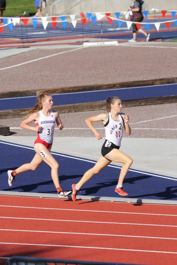 Athlete prepares for pole vault on a track with others watching.