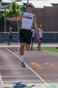 Athlete prepares for pole vault on a track with others watching.