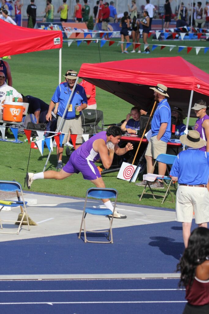 Athlete prepares for pole vault on a track with others watching.