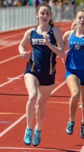 Athlete prepares for pole vault on a track with others watching.