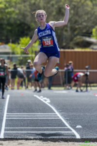 Athlete prepares for pole vault on a track with others watching.
