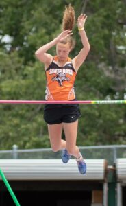 Athlete prepares for pole vault on a track with others watching.
