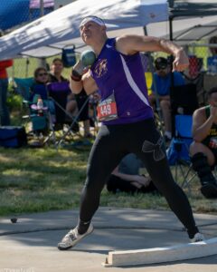 Athlete prepares for pole vault on a track with others watching.