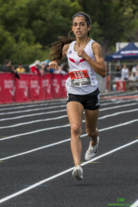 Athlete prepares for pole vault on a track with others watching.