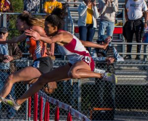 Athlete prepares for pole vault on a track with others watching.