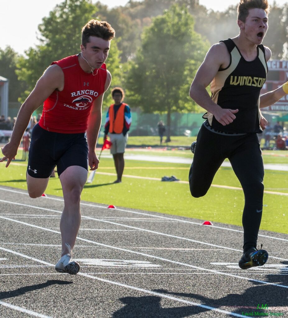Athlete prepares for pole vault on a track with others watching.